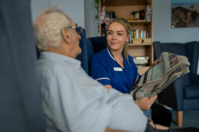 Care Assistant Reading Paper to Resident in the lounge