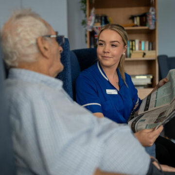 Care Assistant Reading Paper to Resident in the lounge