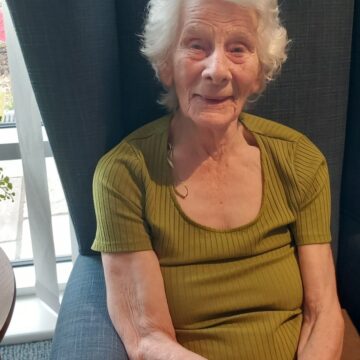Photo of Resident in their chair listening to Peter George singing and playing his guitar