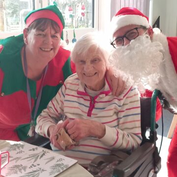 Santa and his elf opening presents with a resident