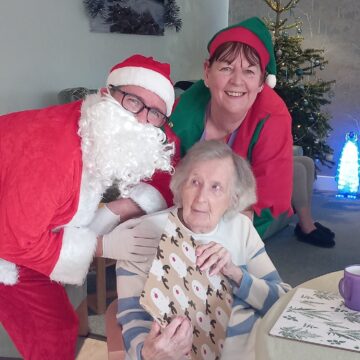 Santa and his elf opening presents with a resident