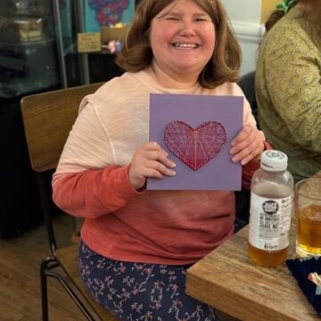 Service User happily showing the card they made with a red love heart on